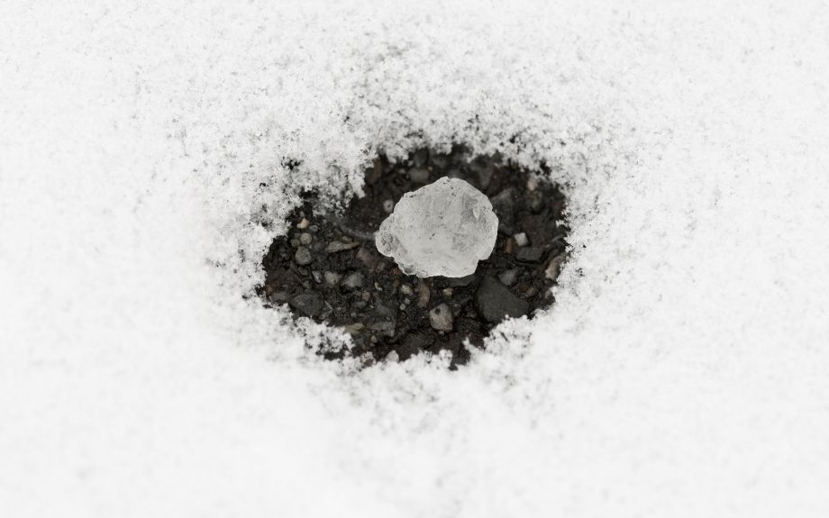 Closeup of a piece of rock salt surrounded by melting snow.