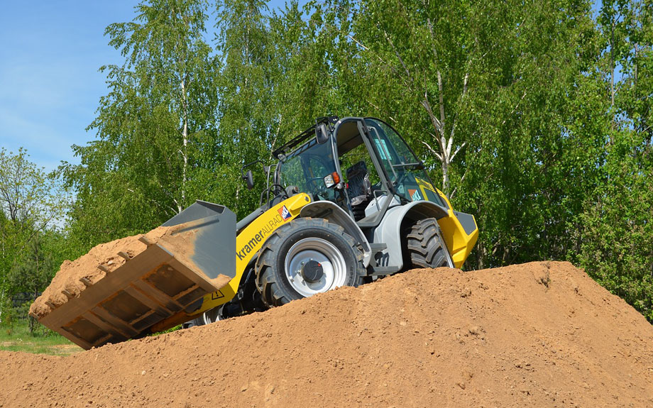 An excavator atop a hill of dirt with trees in the background