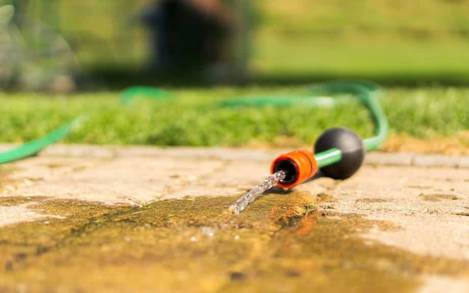 A garden hose with water trickling out on a sidewalk with green grass in the background