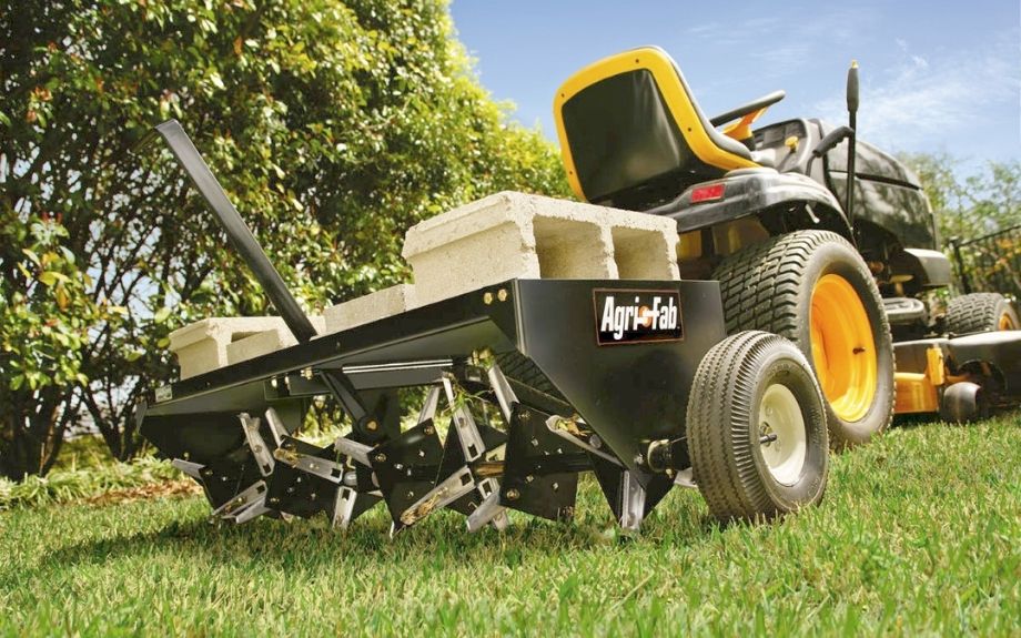 A plug aerator is towed by a lawn tractor on a residential lawn.